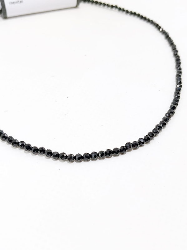 Gargantilla de pequeñas cuentas negras facetadas de turmalina sobre su tarjeta de presentación de Macerox.